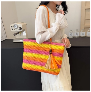 Detailed close-up of rainbow striped straw tote bag with wood bead tassel on shoulder