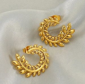 Close-up of golden wheat ear earrings with polished metallic texture on grey silk