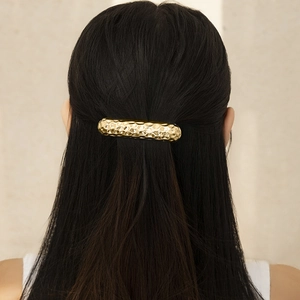 Detail of golden hammered metal hair clip on long black hair with textured finish