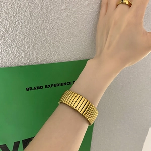 Primer plano de brazalete ancho dorado con textura acanalada vertical y anillo a juego