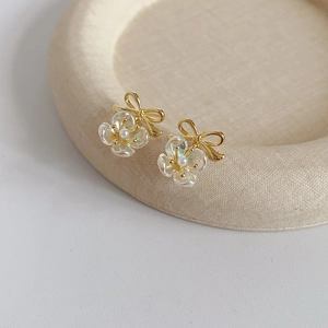 Detailed close-up of French-style gold bow earrings with pearls and transparent flowers