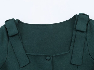 Detail of square neckline and decorative shoulder straps on dark green knit cardigan