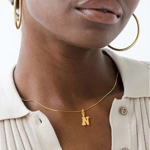 Close-up of a gold capital letter N pendant necklace paired with matching hoop earrings