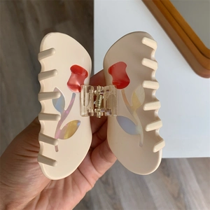 Detailed view of a cream hair claw clip with red tulip patterns and aurora finish leaves