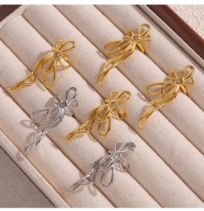 Detailed view of gold and silver bow-shaped rings with zircon inlay on beige velvet tray