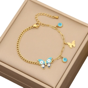 Golden bracelet with blue butterfly and evil eye charms on a beige jewelry box lid