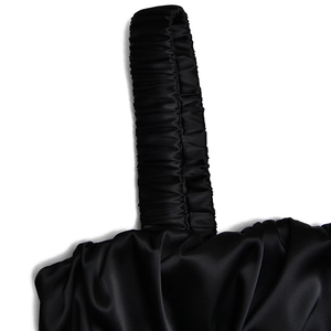 Detail of black satin dress showing pleated shoulder strap and glossy fabric texture