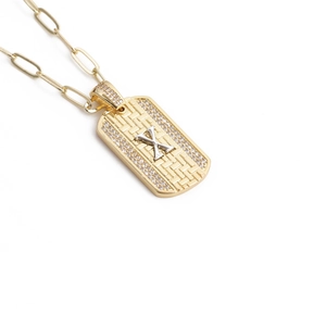 Détail du pendentif rectangle doré avec cristaux pavés et lettre X argentée