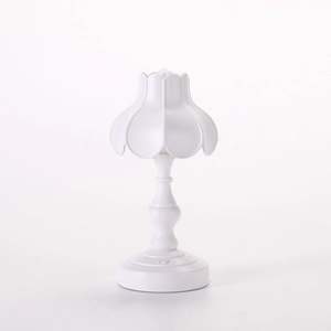 Dettaglio di una lampada da tavolo vintage bianca con paralume a petalo e base intagliata