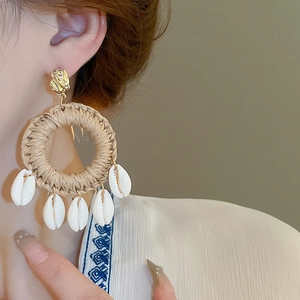 Détail de boucles d'oreilles bohèmes en raphia avec coquillages sur un mannequin