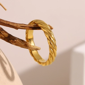 Artistic display of a gold twisted ring hanging on a dry branch with natural lighting