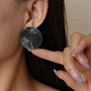 Gros plan de grandes boucles d'oreilles rondes à motif marbré gris sur le modèle