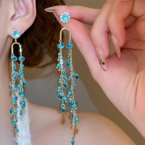 Detail of long gold tassel earrings with light blue crystals and daisy stud attachment