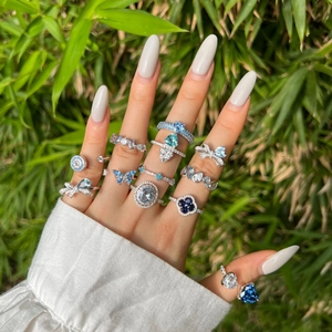 Detail view of silver rings with blue heart and butterfly charms on a hand with bamboo leaves
