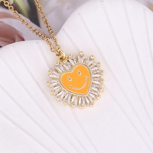 Close-up of golden heart pendant with orange smiley face and zircon border detailing