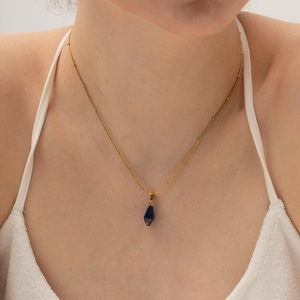 Gold beaded necklace with geometric dark blue crystal pendant on a model neck
