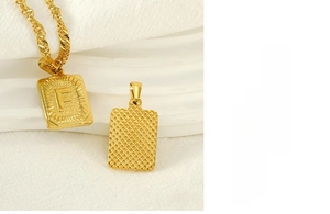 Detail of gold stainless steel necklace with square pendant showing letter F and grid texture