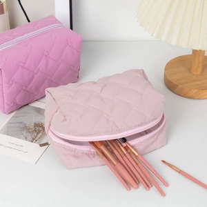 Detail of quilted cosmetic bags with metal zippers and brushes in soft pink fabric