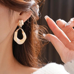 Close-up of model wearing oval resin earrings with metallic irregular white stone pendants