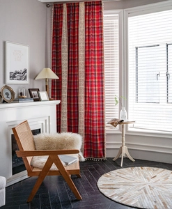 Detail of red plaid curtain with beige lace trim and fringe hanging in cozy room