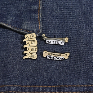 Detailed close-up of three medical skeleton enamel pins on blue denim fabric