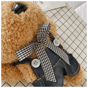 Close-up of teddy bear plush bag with denim overalls and black-white checkered bow tie