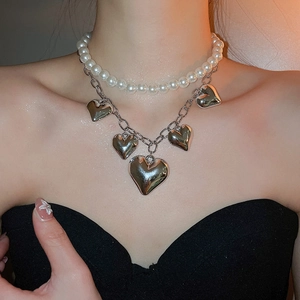 Detail of layered pearl and silver chain necklace with heart pendants on model