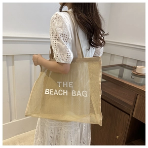 Detailed view of the large beige mesh beach tote bag carried by a model in a minimalist room