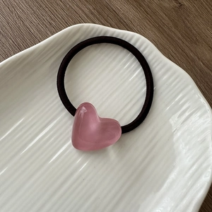 Detail of a pink heart resin pendant hair tie on a white striped ceramic plate