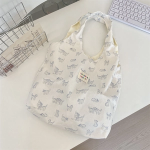 Close-up of cat print canvas tote bag with colorful embroidered label on white desk