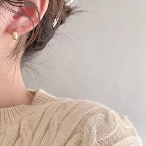 Close-up of a model wearing golden teardrop-shaped sterling silver hoop earrings with a polished finish