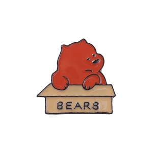 Close-up of a cute red bear enamel pin sitting inside a yellow BEARS cardboard box