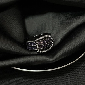Macro detail of belt buckle ring featuring purple gemstones on black satin fabric