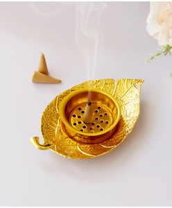 Detailed view of leaf-shaped gold incense burner with burning cone and smoke texture
