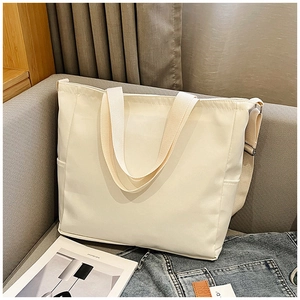 Detail of cream canvas tote bag with adjustable strap and side pocket on a sofa