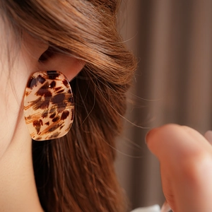 Close-up of a large oval resin earring with brown leopard print on a model's ear