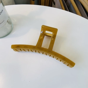 Close-up of amber large shark hair claw clip with strong metal spring on white desk