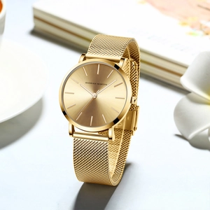 Close-up of golden women's watch with metal mesh strap on a cozy desk with flowers