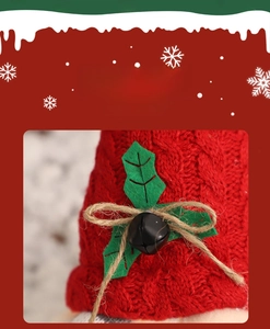 Dettaglio del cappello da gnomo natalizio in maglia rossa con foglie di agrifoglio e campanello