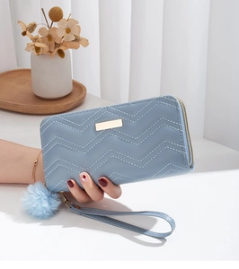 Close-up of wavy quilted long wallet with golden metal plate and blue pompom charm