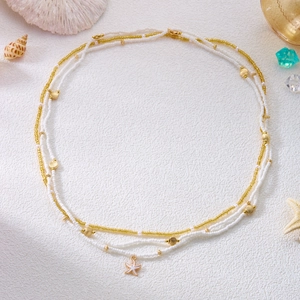 Detail of beaded shell necklace with starfish pendant and golden shell charms on white fabric