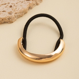 Macro shot of gold curved metal accent on black elastic hair tie with minimalist design