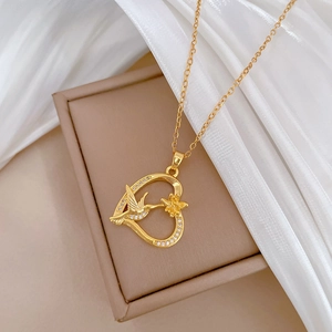 Macro detail of a gold hummingbird heart pendant with crystal inlay on a gift box