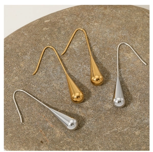 Detailed close-up of long teardrop earrings in gold and silver finish on natural stone