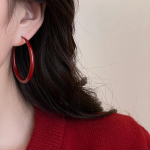 Close-up of a large glossy red geometric round hoop earring worn by a female model