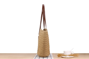 Side view of large woven tote bag with brown leather straps on a wooden table
