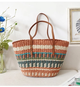 Detail of multi-color striped handmade straw tote bag with brown leather handle on sofa
