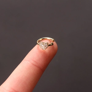 Macro view of a tiny golden heart ear cuff with white zircon stones on a fingertip