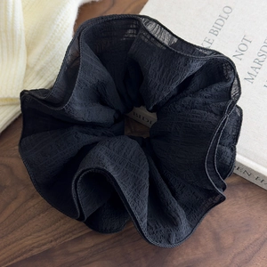 Macro detail of oversized black ruffle scrunchie showing pleated chiffon fabric texture
