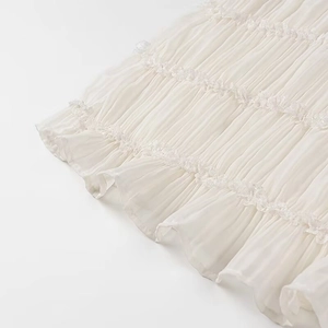 Dettaglio del tessuto in chiffon plissettato bianco e pizzo delicato su un abito elegante